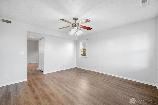 unfurnished room with visible vents, ceiling fan, wood finished floors, and baseboards