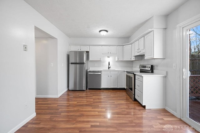 kitchen with wood finished floors, a sink, white cabinetry, and stainless steel appliances