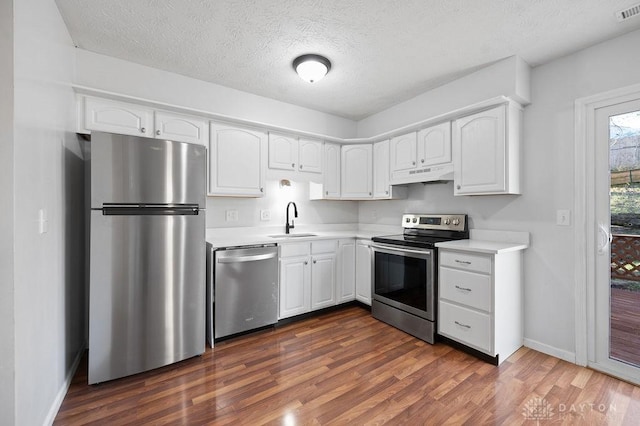 kitchen featuring a sink, light countertops, dark wood finished floors, under cabinet range hood, and stainless steel appliances