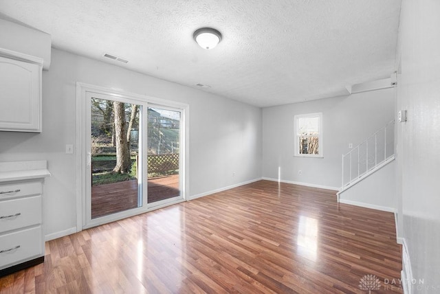 unfurnished living room with baseboards, a textured ceiling, stairs, visible vents, and wood finished floors