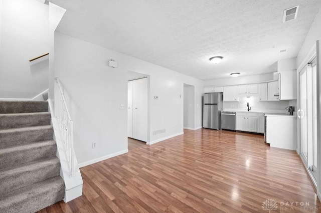 unfurnished living room featuring visible vents, baseboards, stairway, and light wood-style floors