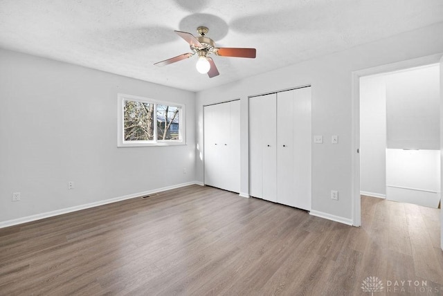unfurnished bedroom featuring ceiling fan, visible vents, wood finished floors, multiple closets, and baseboards