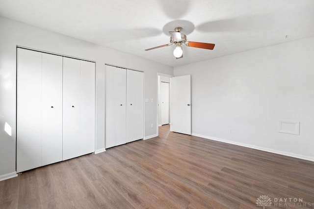 unfurnished bedroom featuring multiple closets, ceiling fan, wood finished floors, and baseboards
