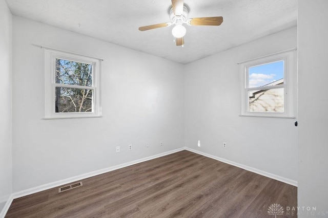 empty room featuring a ceiling fan, baseboards, dark wood-style floors, and visible vents