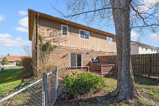 back of property featuring brick siding, fence, a wooden deck, and a lawn