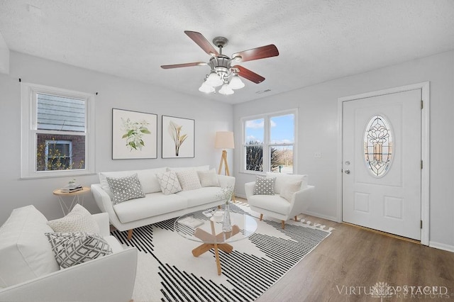 living area featuring a textured ceiling, wood finished floors, ceiling fan, and visible vents