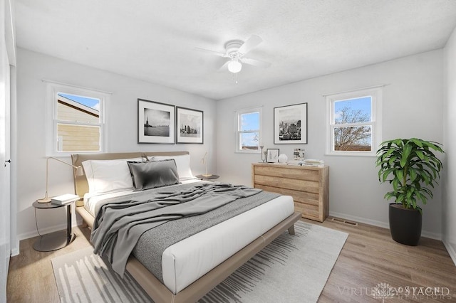 bedroom featuring light wood-style flooring, baseboards, visible vents, and ceiling fan