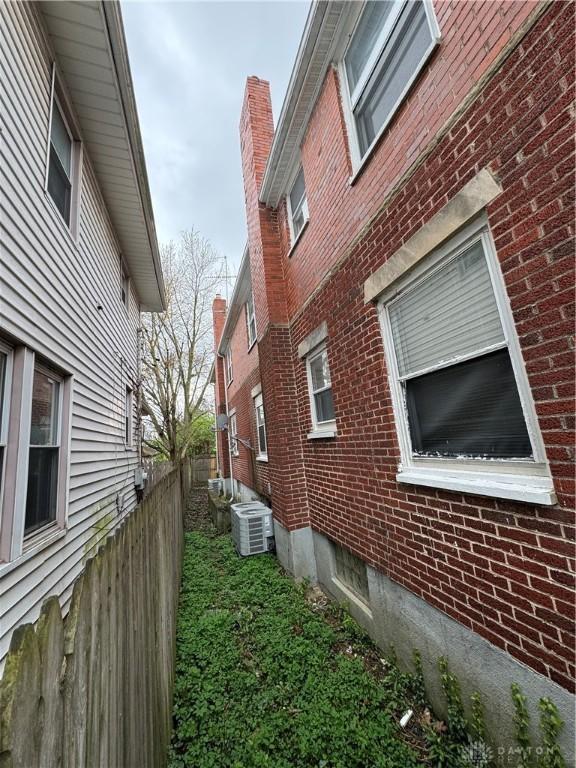 view of property exterior featuring fence, brick siding, and central AC