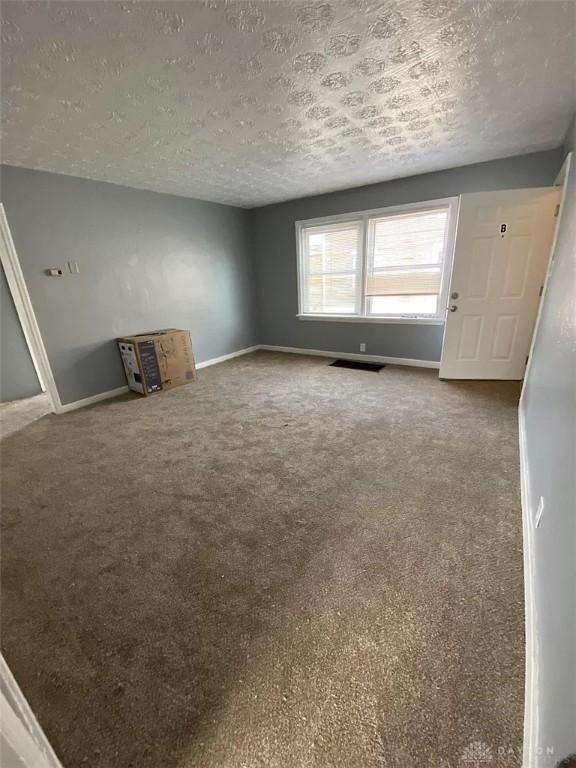 unfurnished living room with baseboards, a textured ceiling, visible vents, and carpet