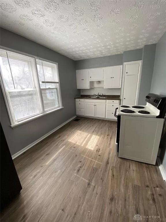 kitchen featuring a sink, white cabinetry, wood finished floors, white electric range oven, and dark countertops