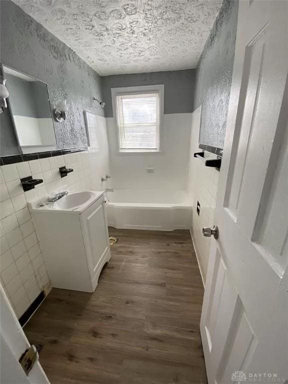 bathroom with vanity, shower / washtub combination, wood finished floors, a textured ceiling, and tile walls