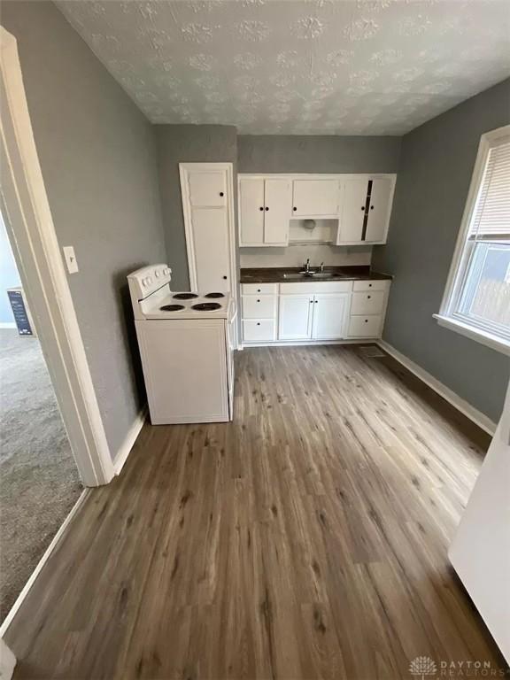 kitchen with white range with electric cooktop, dark wood-style floors, baseboards, dark countertops, and white cabinets