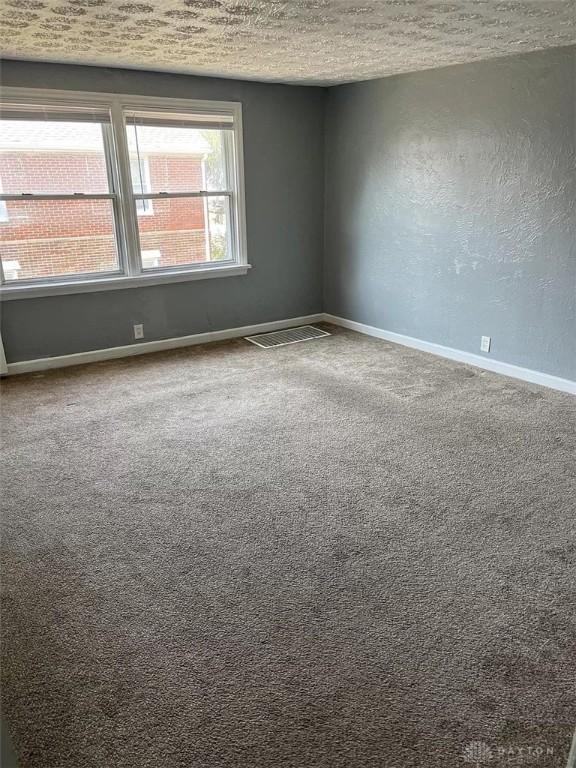 carpeted empty room with visible vents, a textured wall, baseboards, and a textured ceiling