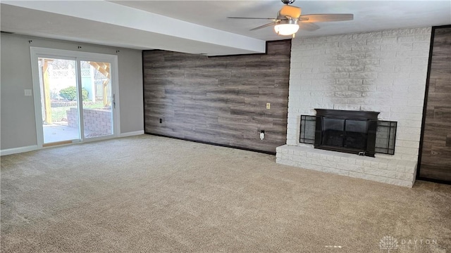 unfurnished living room featuring a fireplace, wooden walls, ceiling fan, and carpet