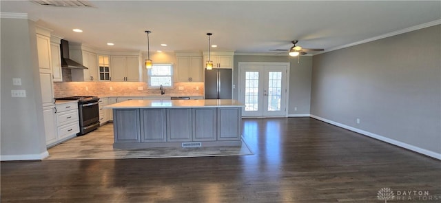 kitchen featuring light countertops, a ceiling fan, wall chimney exhaust hood, appliances with stainless steel finishes, and a center island