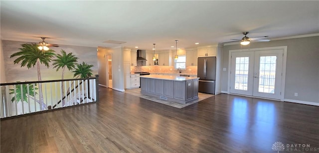 kitchen featuring a sink, freestanding refrigerator, white cabinetry, wall chimney range hood, and ceiling fan