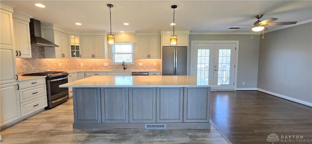 kitchen with light countertops, a sink, wall chimney range hood, a ceiling fan, and appliances with stainless steel finishes
