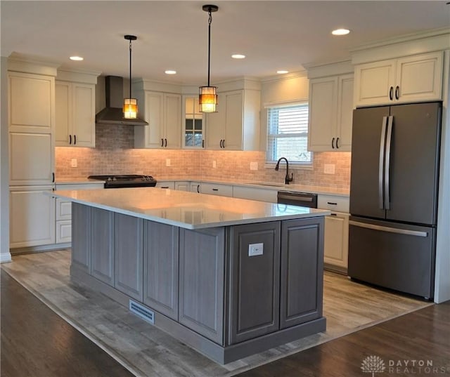 kitchen featuring white cabinetry, wall chimney range hood, a sink, light wood finished floors, and freestanding refrigerator