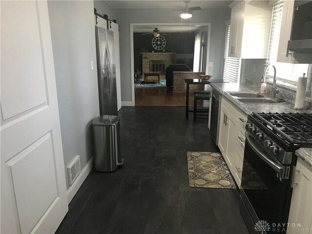 7581 Lockwood St, Dayton, OH 45415 - kitchen with appliances with stainless steel finishes, white cabinetry, a ceiling fan, a fireplace, and range hood