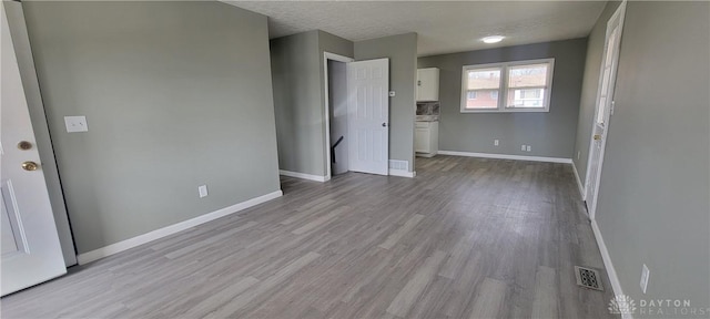 unfurnished room with baseboards, visible vents, a textured ceiling, and wood finished floors