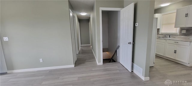 hall with light wood finished floors, baseboards, and a sink
