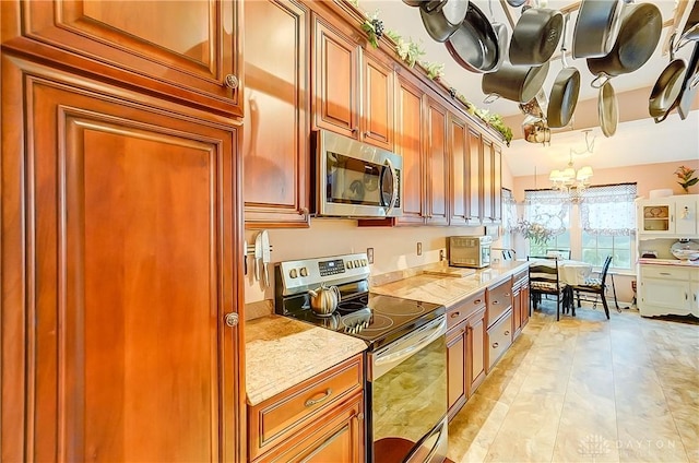 3949 E Summit Ridge Dr, Beavercreek, OH 45430 - kitchen with stainless steel appliances, a chandelier, brown cabinetry, and light stone countertops