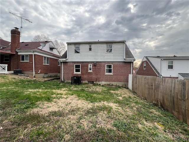 back of property featuring central AC, fence, brick siding, and a yard