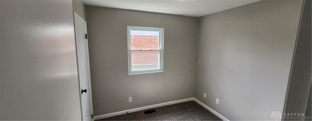 spare room with dark colored carpet and baseboards