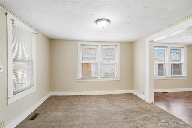empty room featuring carpet, baseboards, a healthy amount of sunlight, and visible vents