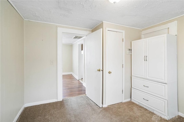 unfurnished bedroom featuring light carpet, a textured ceiling, baseboards, and visible vents