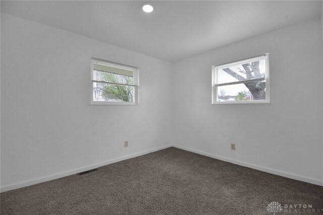 empty room featuring dark carpet, baseboards, visible vents, and a healthy amount of sunlight