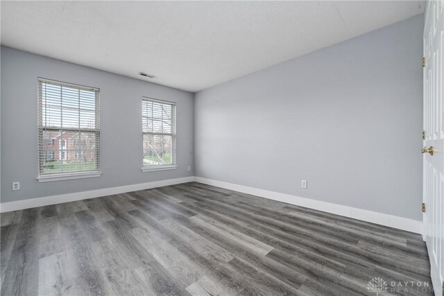 empty room featuring wood finished floors, baseboards, and visible vents