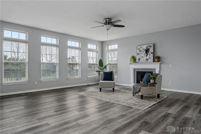 living area with baseboards, a lit fireplace, a ceiling fan, and dark wood finished floors