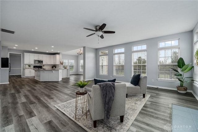 living room with dark wood-style flooring, visible vents, baseboards, recessed lighting, and ceiling fan with notable chandelier