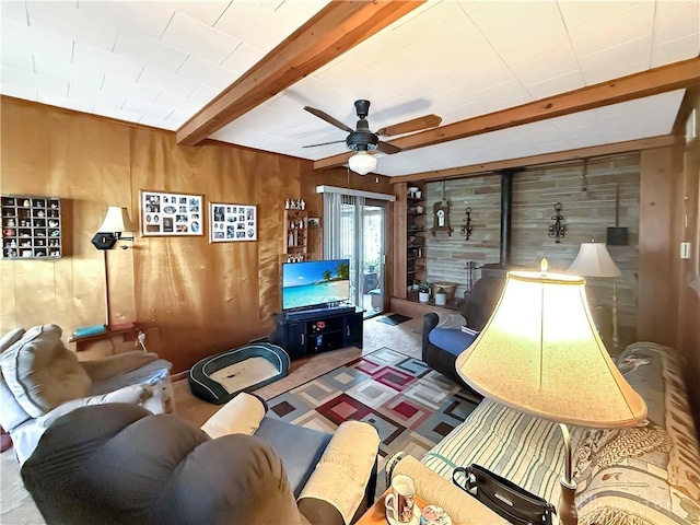 living room with carpet, wooden walls, ceiling fan, beam ceiling, and a wood stove