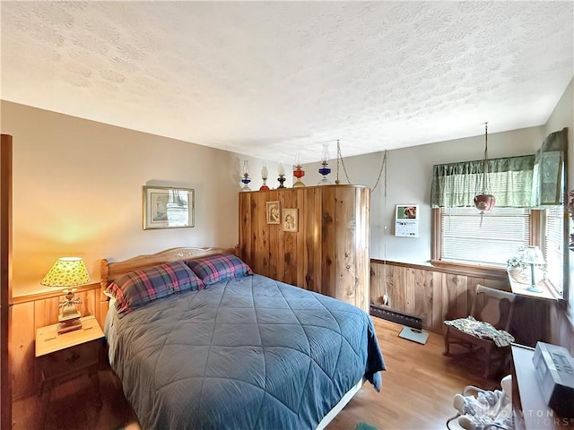 bedroom with a textured ceiling, wood finished floors, wainscoting, and wood walls