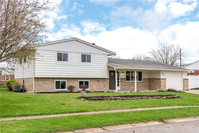 tri-level home with cooling unit, a front yard, a garage, and brick siding
