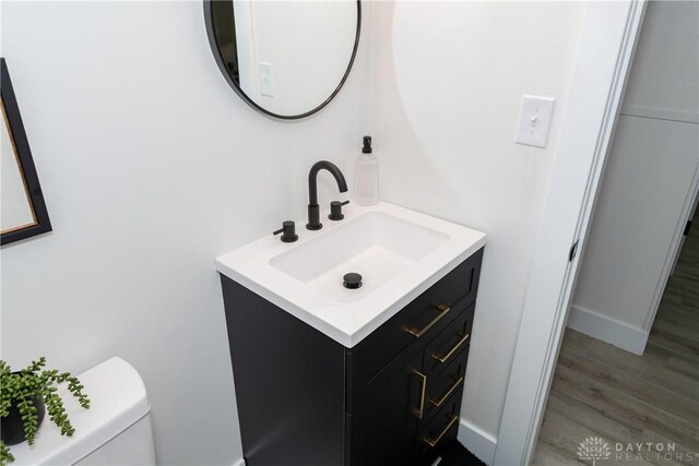 half bath with toilet, vanity, and wood finished floors