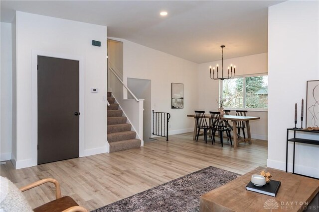 living area featuring lofted ceiling, stairway, baseboards, a chandelier, and light wood-style flooring
