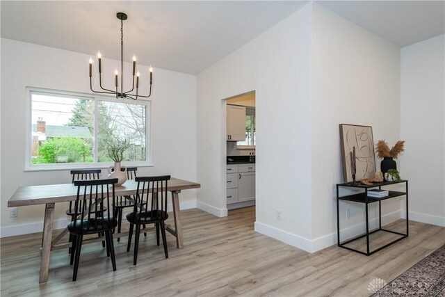 dining space with light wood-style flooring, a notable chandelier, and baseboards
