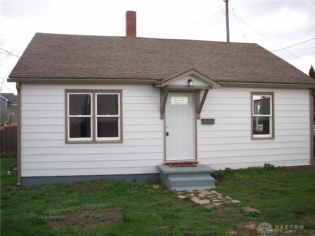 bungalow-style home with a front yard, fence, roof with shingles, and a chimney