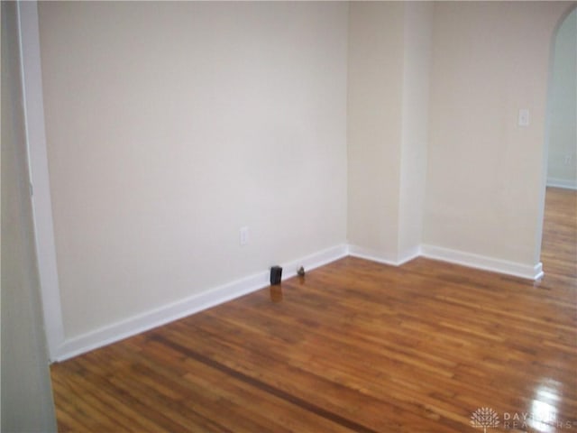 empty room with arched walkways, baseboards, and wood finished floors