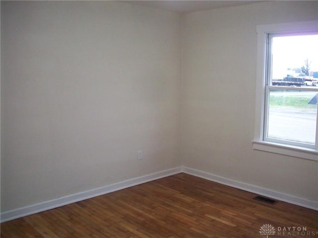 empty room featuring baseboards, visible vents, and dark wood-style floors