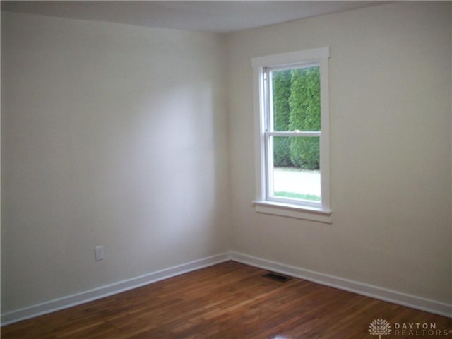 empty room featuring dark wood-type flooring, visible vents, and baseboards