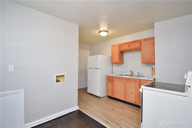 kitchen featuring light countertops, light wood-style flooring, white appliances, baseboards, and a sink