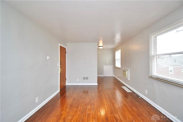 spare room featuring heating unit, baseboards, visible vents, and hardwood / wood-style floors