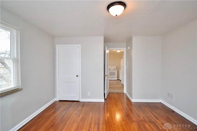 unfurnished bedroom featuring baseboards, wood finished floors, and freestanding refrigerator