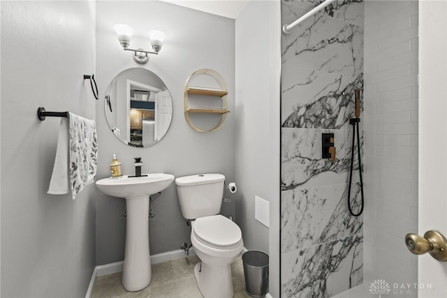 bathroom featuring toilet, tile patterned floors, a tile shower, and baseboards