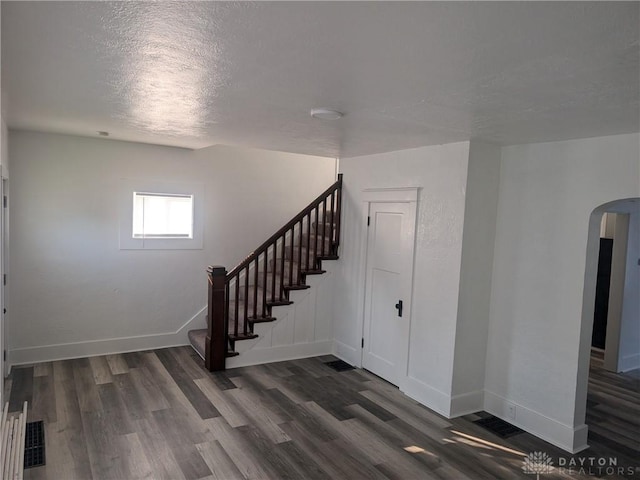 interior space with arched walkways, dark wood-type flooring, baseboards, and stairs