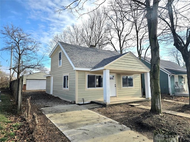 bungalow featuring covered porch, an outbuilding, concrete driveway, and a shingled roof